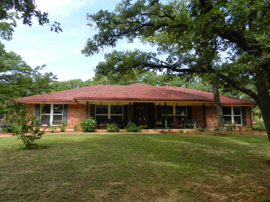 a brick house with a red roof and a large tree