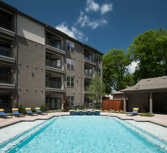 a swimming pool with lounge chairs and trees in the background